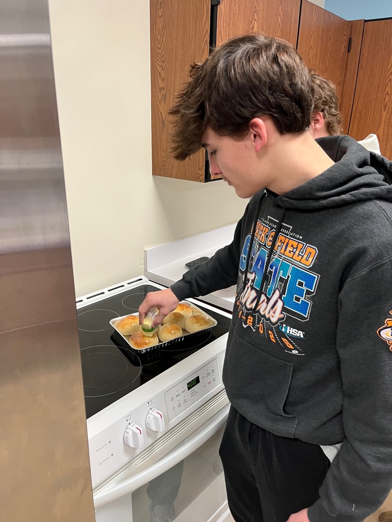 A student is buttering a pan of rolls. 