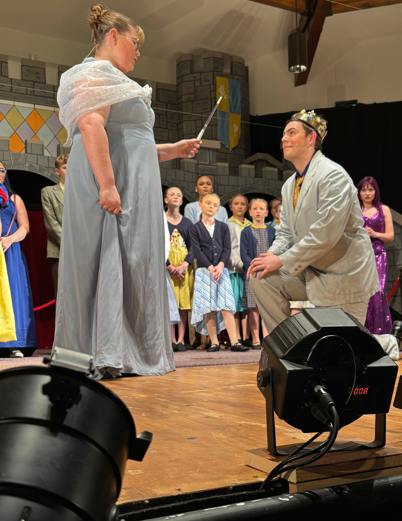 A fairygodmother is casting a spell with a wand on another character with a crown.