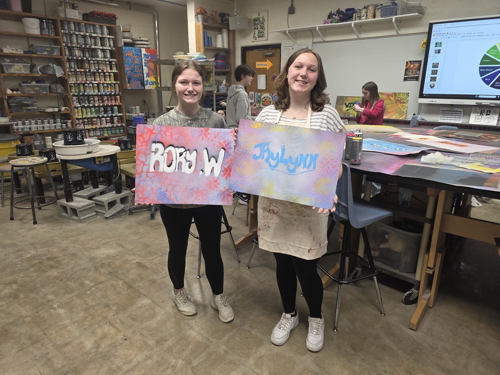 Two students are showing their cardboar piece with graffiti art.