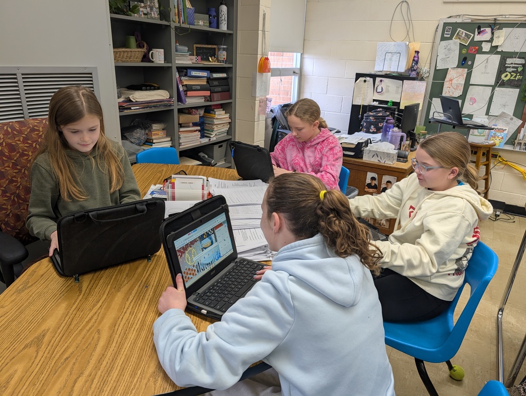 A group of four students are sitting at a table together. Each is working on a shared document on their Chromebook. 