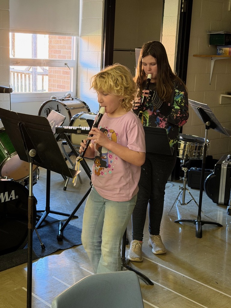 Two students are standing in front of music stands playing the recorder.