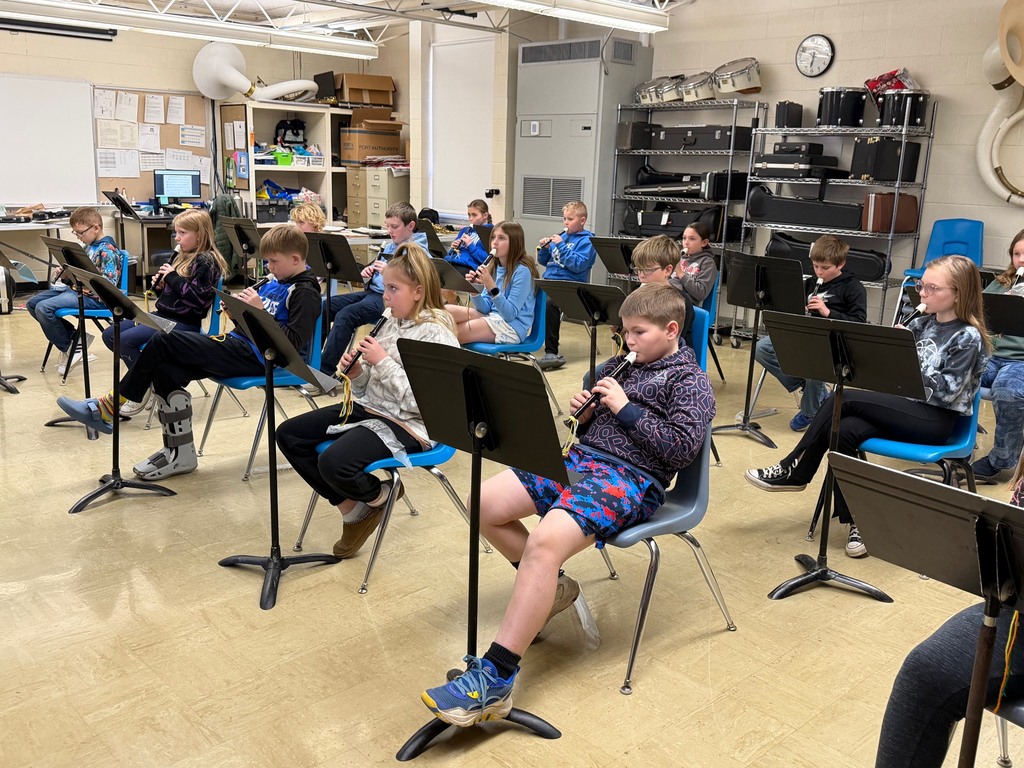 The class is sitting in their chairs with a stand in front of them and playing the new note.