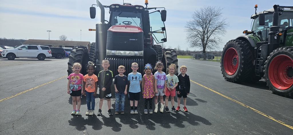 A group of 9 students are standing in front of a tractor.
