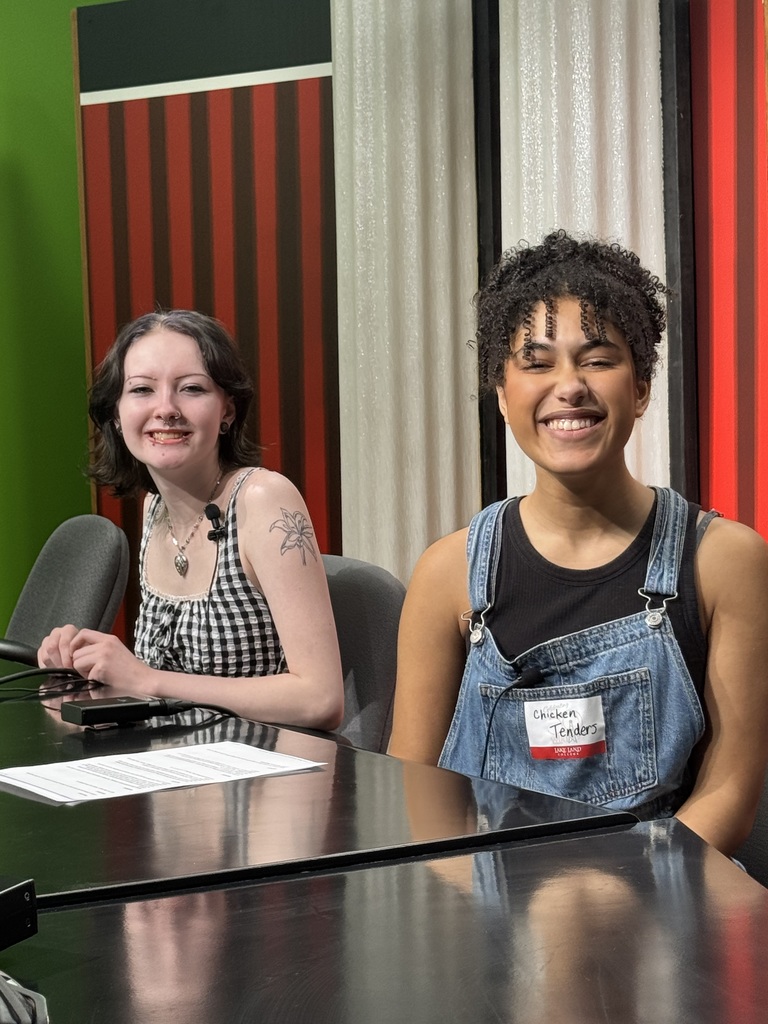 Two students are sitting at the desk for a news broadcast. 