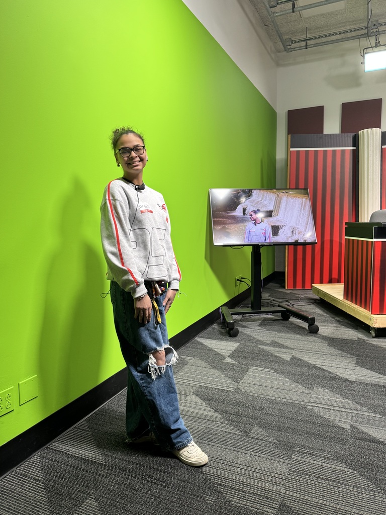 A student is standing in front of a green screen. 
