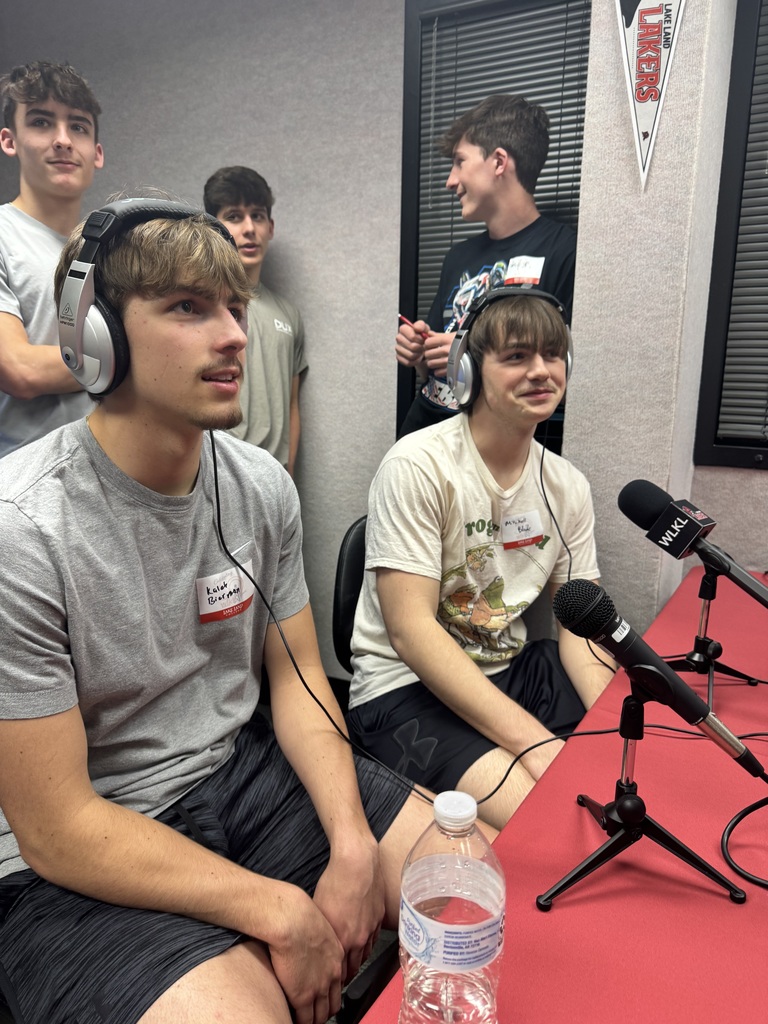 Two students are sitting in front of microphones and wearing headphones. They are being interviewed for the radio.