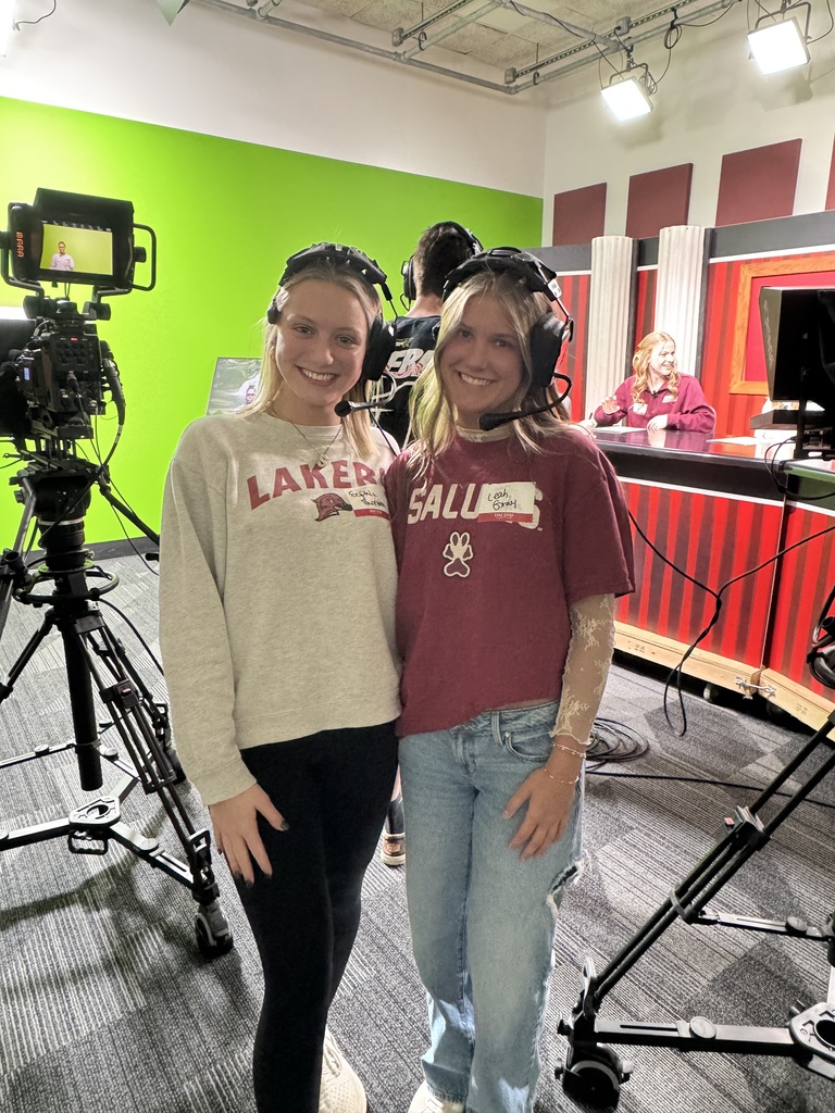 Two students are standing with cameras. They are wearing headsets. 