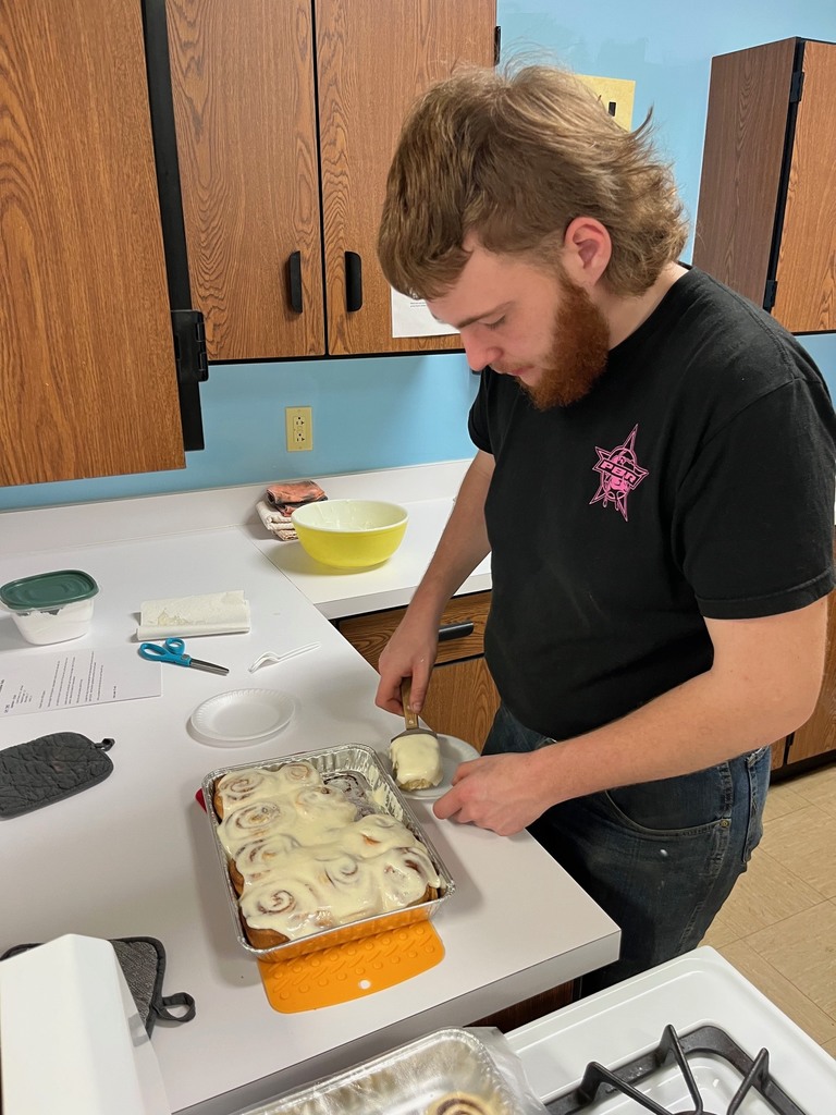 A student is dishing up a cinnamon roll from his pan. 