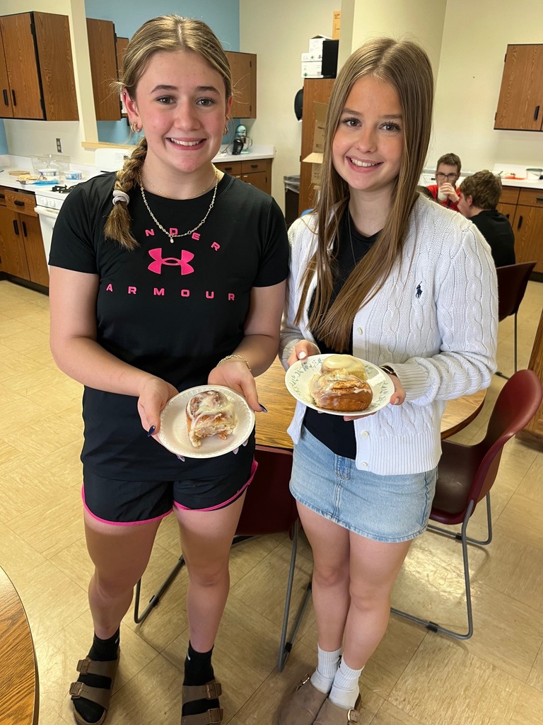 Two students are standing with a plate with a cinnamon roll. 