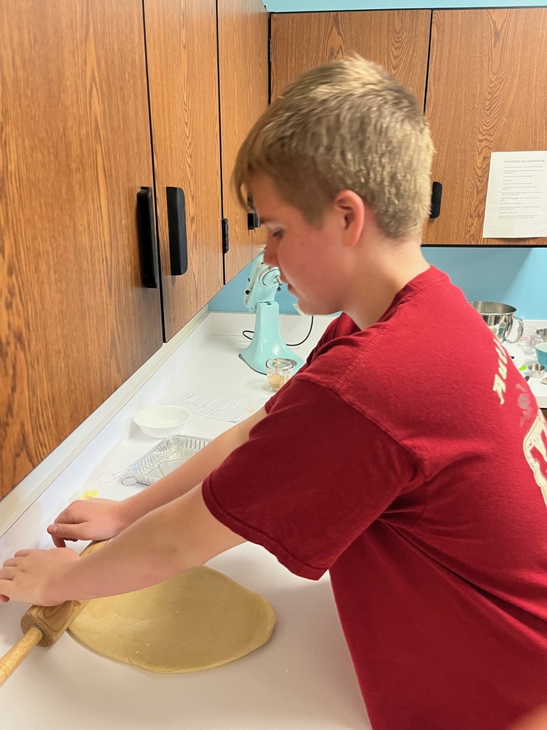 A student is rolling dough with  a rolling pin.