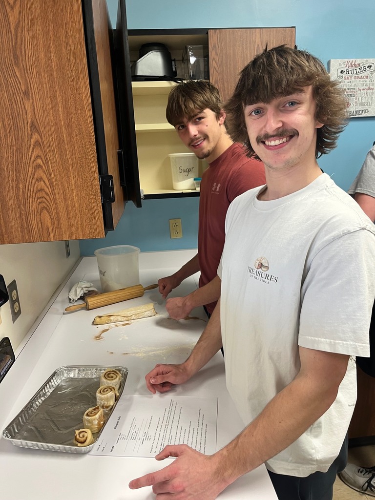 Two students are placing rolls in a pan. 