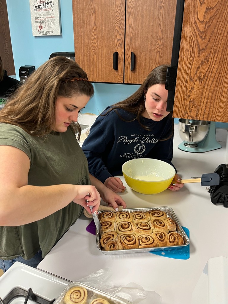 Two students are icing the cinnamon rolls. 