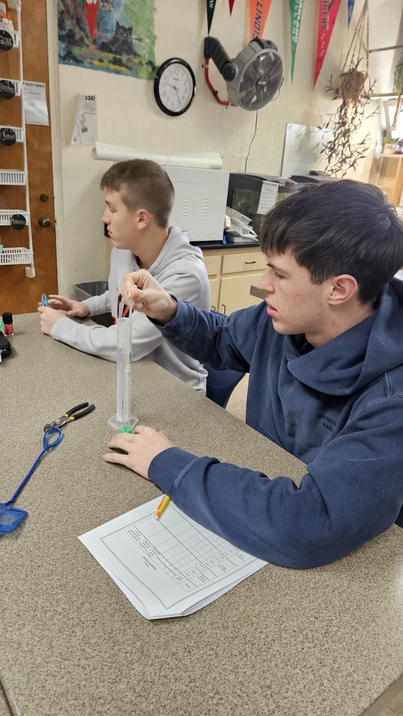 One student is using an eye dropper to get water out of a graduated cylinder. Another is using a tweezer to pick up something.