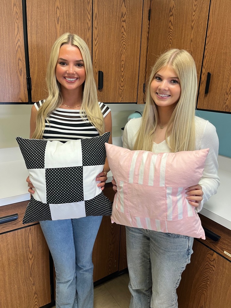 Two students are holding the pillow they made.
