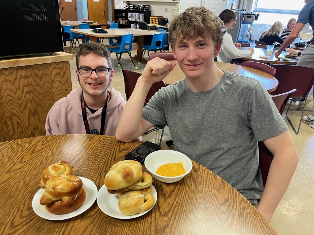 Two students are sitting with a plate of pretzels and a bowl of cheese sauce.