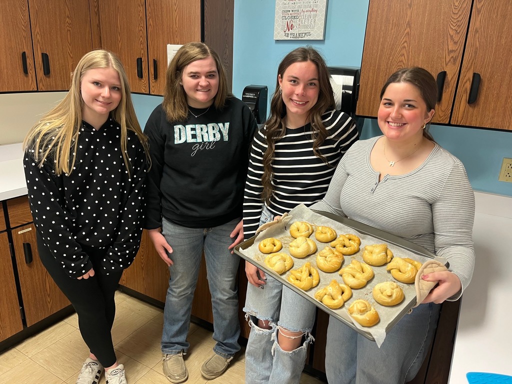 Four students are displaying their cooking sheet with pretzels just out of the oven.