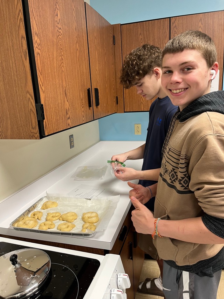 Two students are shaping pretzels and placing them on the cooking sheet.