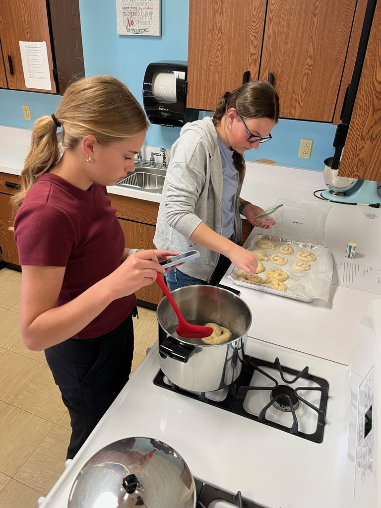 One student is giving the pretzels a baking soda bath. The other is placing them on the cooking sheet.