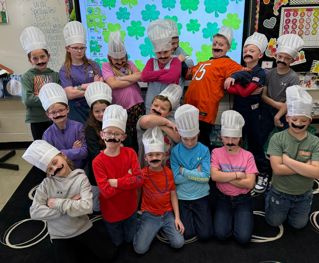 The class is in three rows. They are wearing chef hats and stick on mustaches.