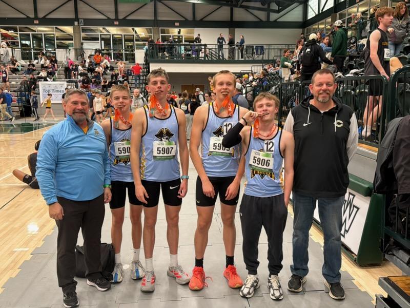 The 4x800 team and two coaches are pictured. The team is biting their medals. 