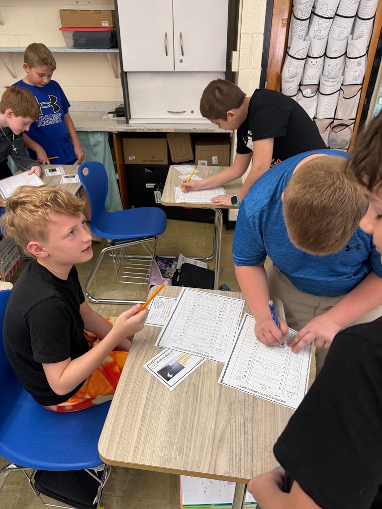 Three students are gathered around a desk solving a task card.