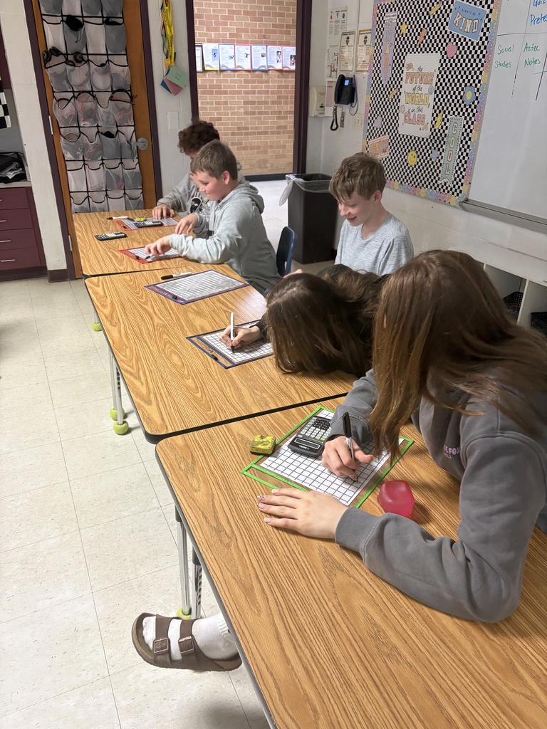 Four students are working on a math problem on a white board.