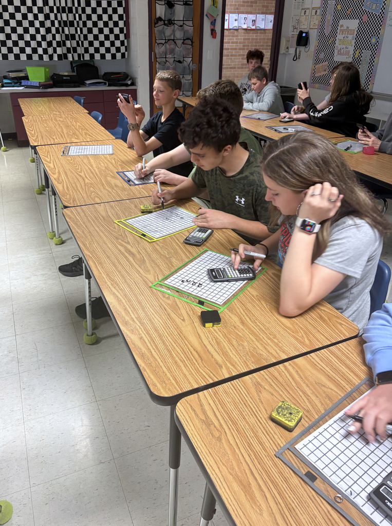 Four students are working on a math problem on a white board.