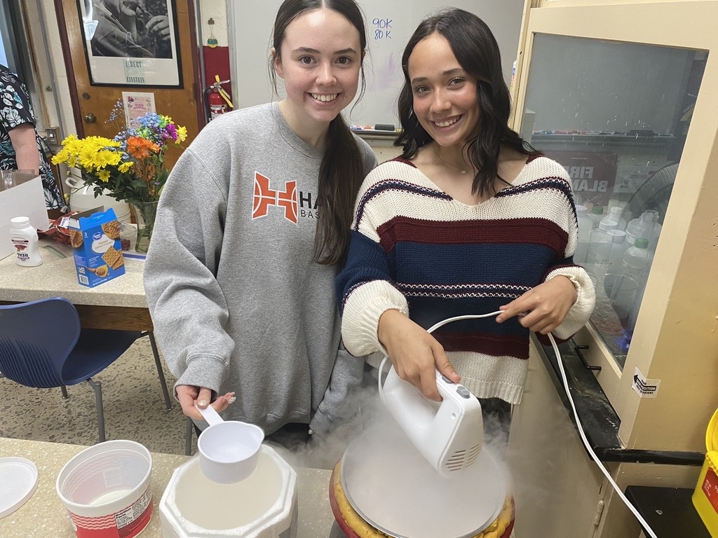 Two students are making ice cream. One is mixing the ice cream, while the other adds the liquid nitrogen.