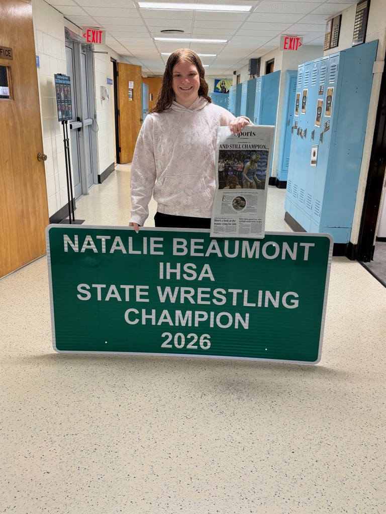 A student is holding the sign that reads Natalie Beaumont IHSA State Wrestling Champion 2026 and holding the newspaper.