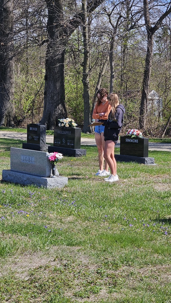 Two students are standing near a gravestone with a clipboard collecting data.
