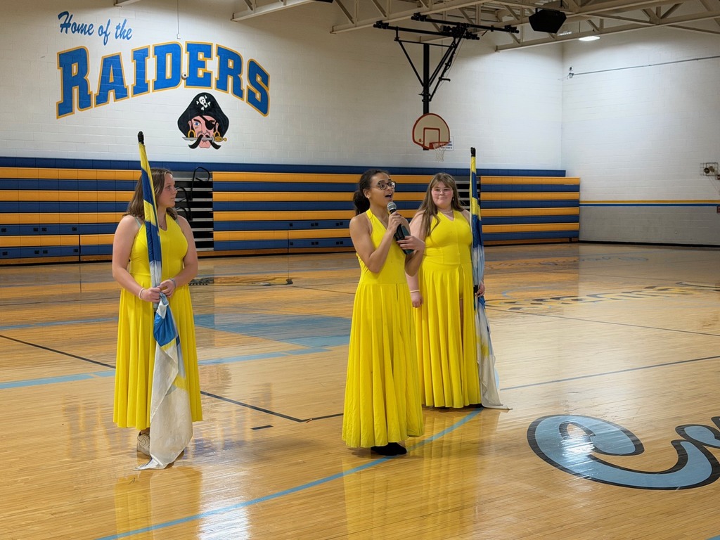 One of the three color guard members are speaking to the crowd about color guard.