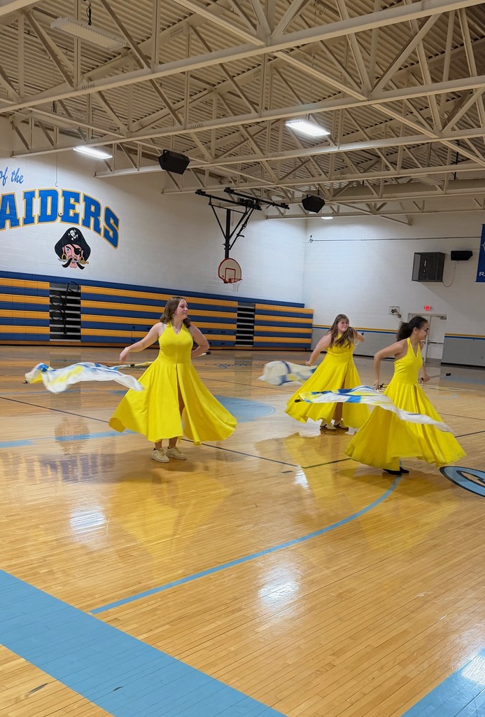 Three color guard members are twirling the flag around their waist.