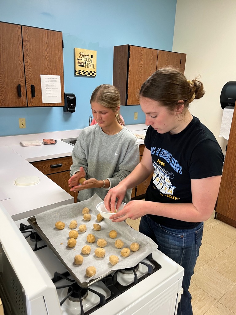 Two students are rolling dough into balls and placing them on the baking sheet.