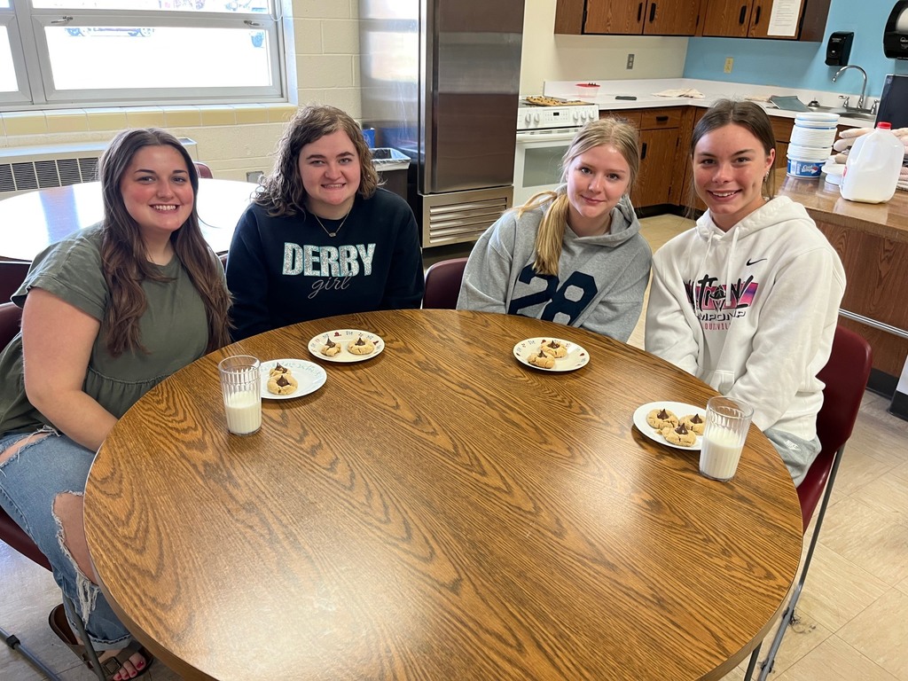 Four students sitting around a table with plates of cookies and glasses of milk.