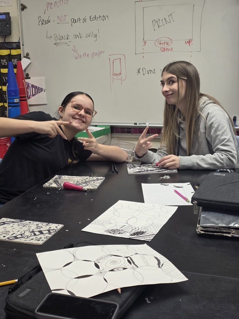 Two students are holding up peace fingers while working on their print.