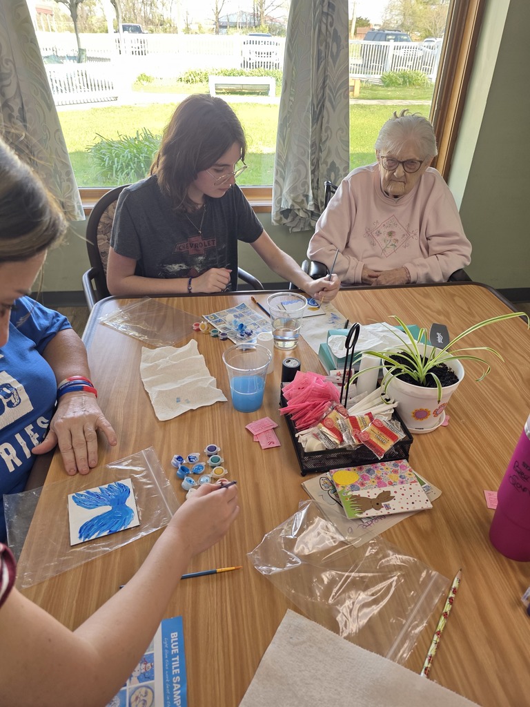 A student is helping a nursing home resident with painting a tile.