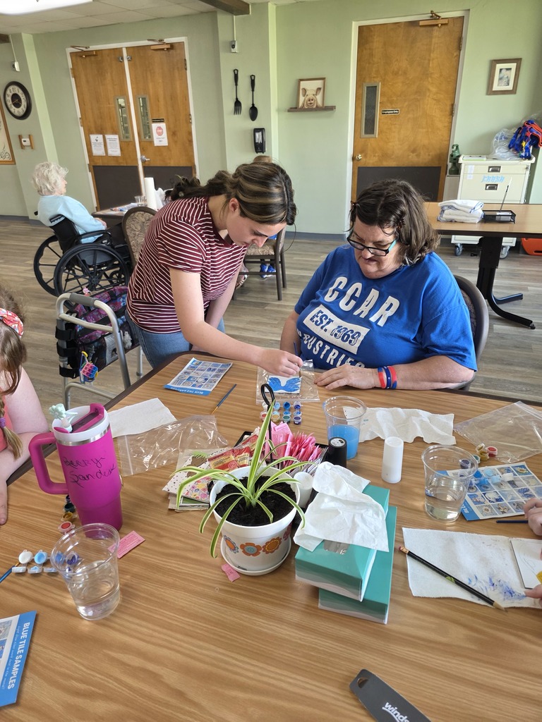 A student is helping a nursing home resident with painting a tile.