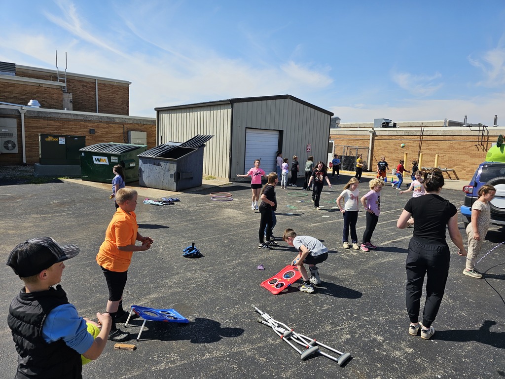 Students are playing a variety of outdoor activities like bean bag toss. 
