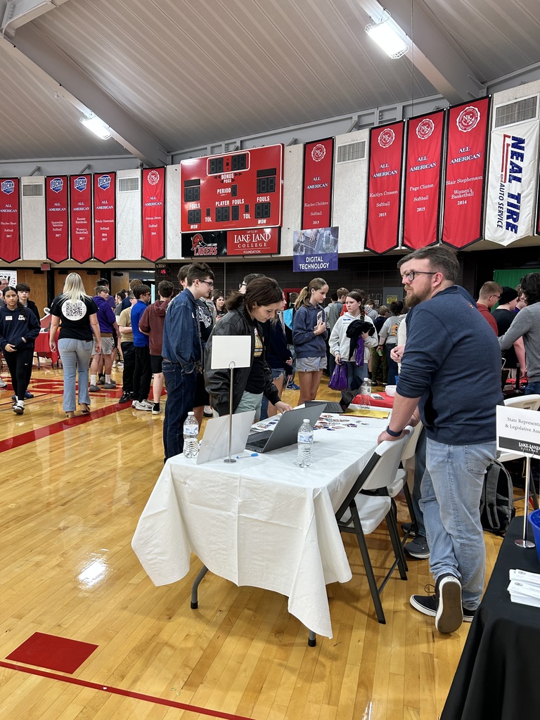 A group of students are checking out what is on a presenter's table.