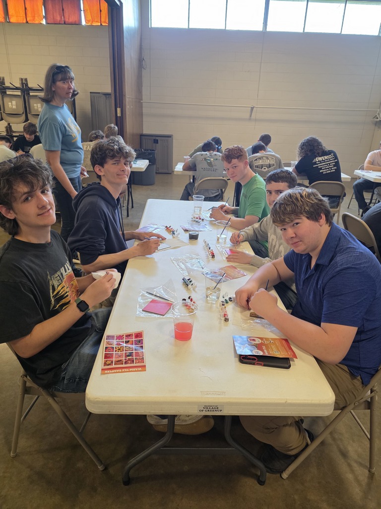 Five students are sitting at the tables painting their tiles.
