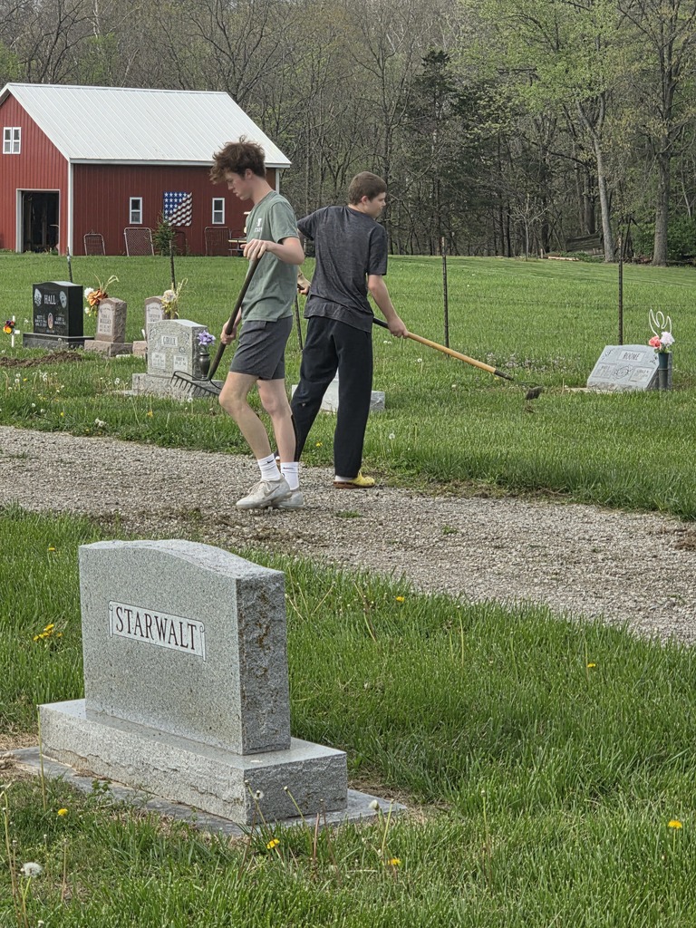 Two students are raking at the cemetery.
