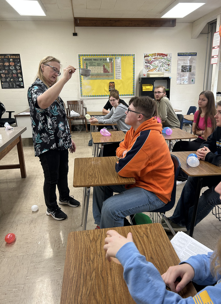 A teacher is holding a cup that is steaming. The class is watching.