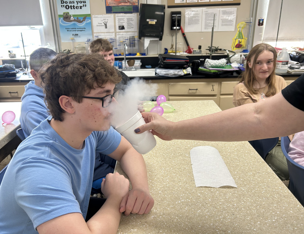 A teacher is holding a cup of steaming nitrogen for a student to see.