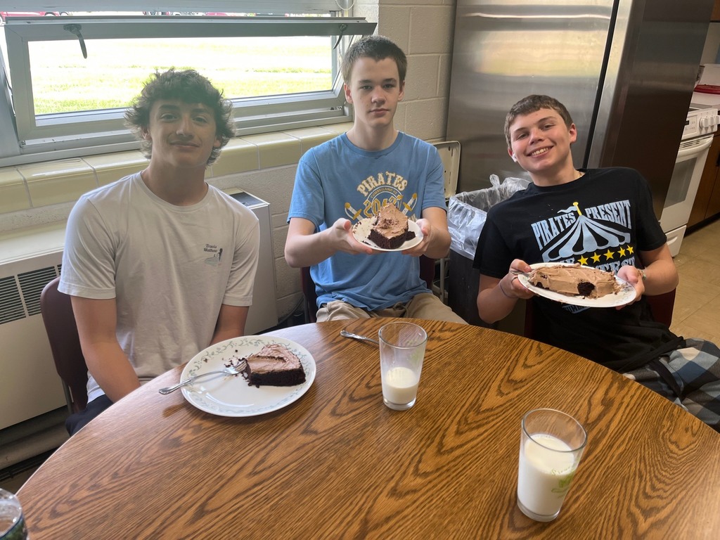 Three students each have a plate with a slice of cake and a glass of milk. 