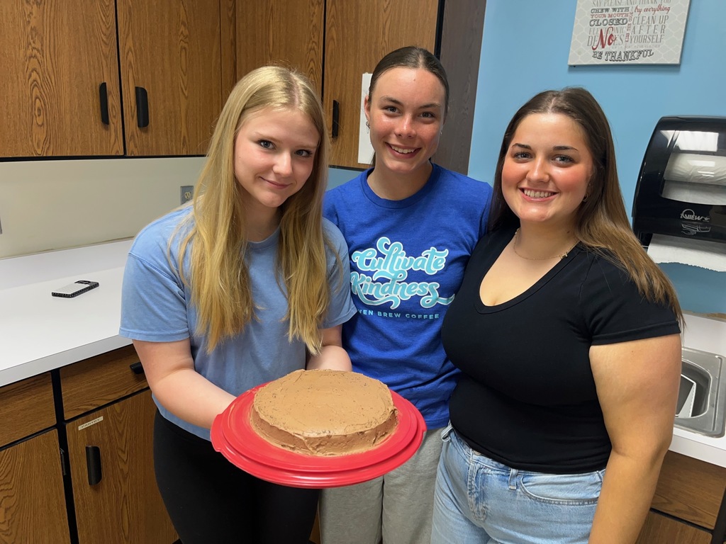 Three students are displaying thier iced chocolate cake. 