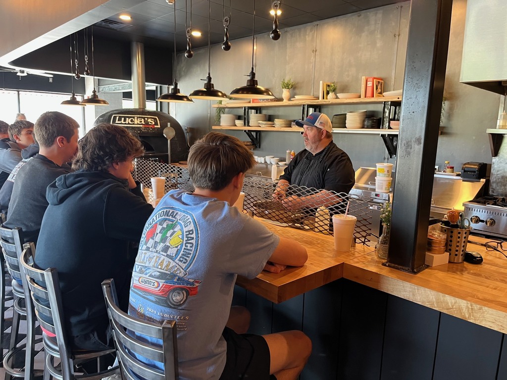 Students are sitting at the bar area and the chef is talking to him. 