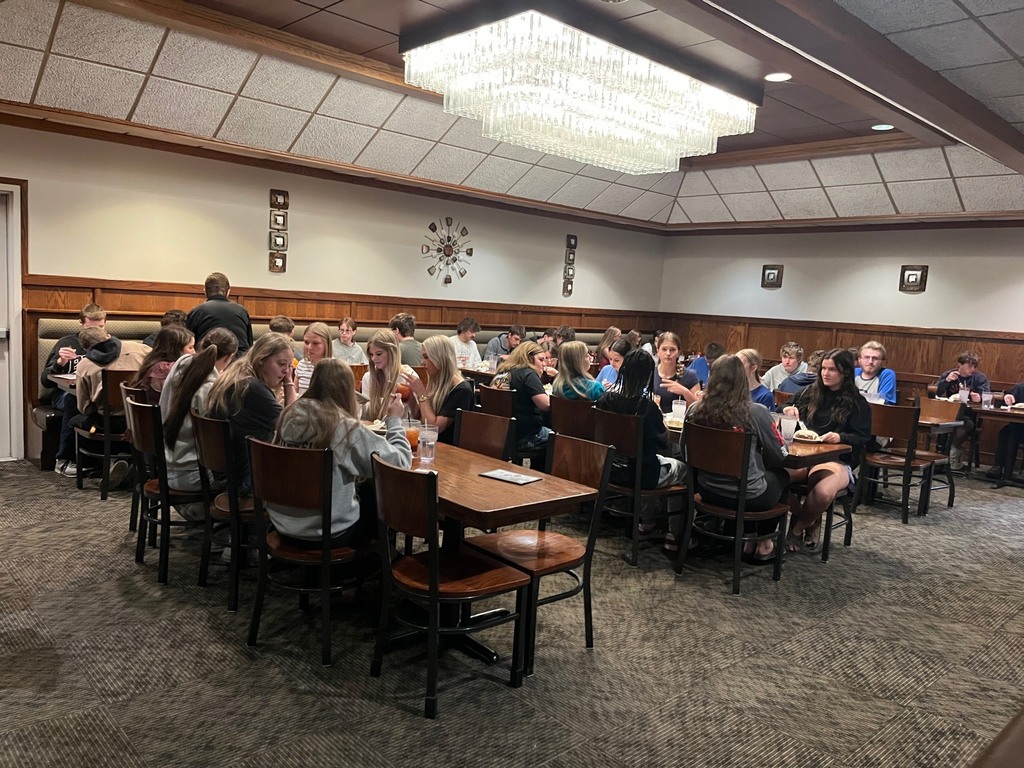 Students are sitting at dinning tables in a restaurant. 