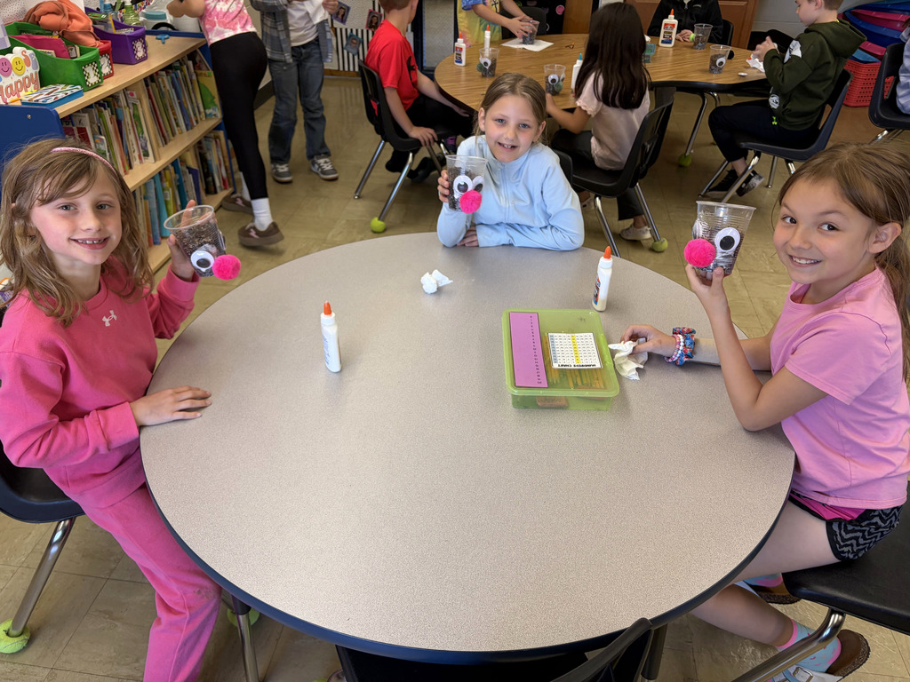 Three students are holding their plant cups after they added eyes and a nose. 