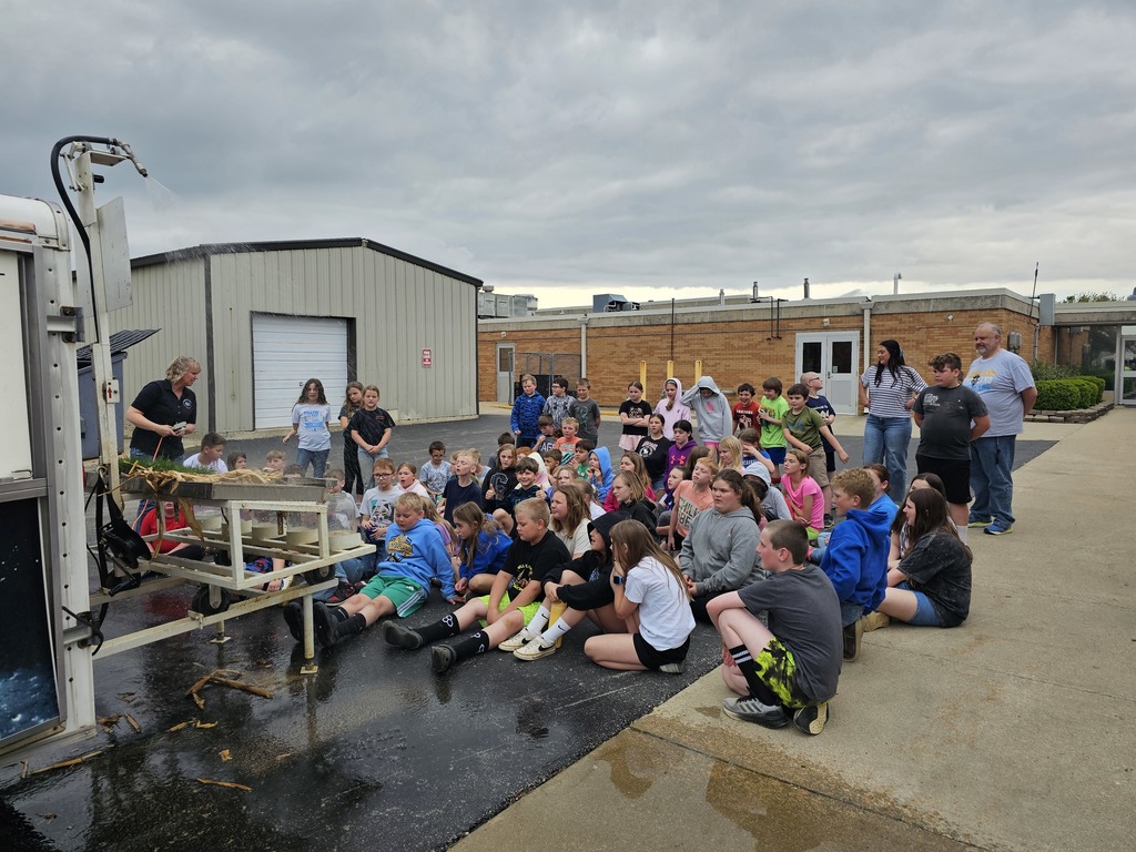 A group of students are outside sitting on the ground for a water and soil presentation. 