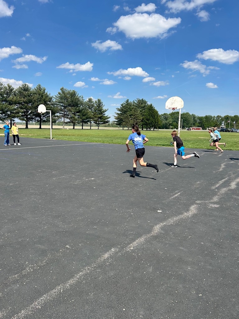 Four students are racing to the tic tac toe board to place their bean bag. 